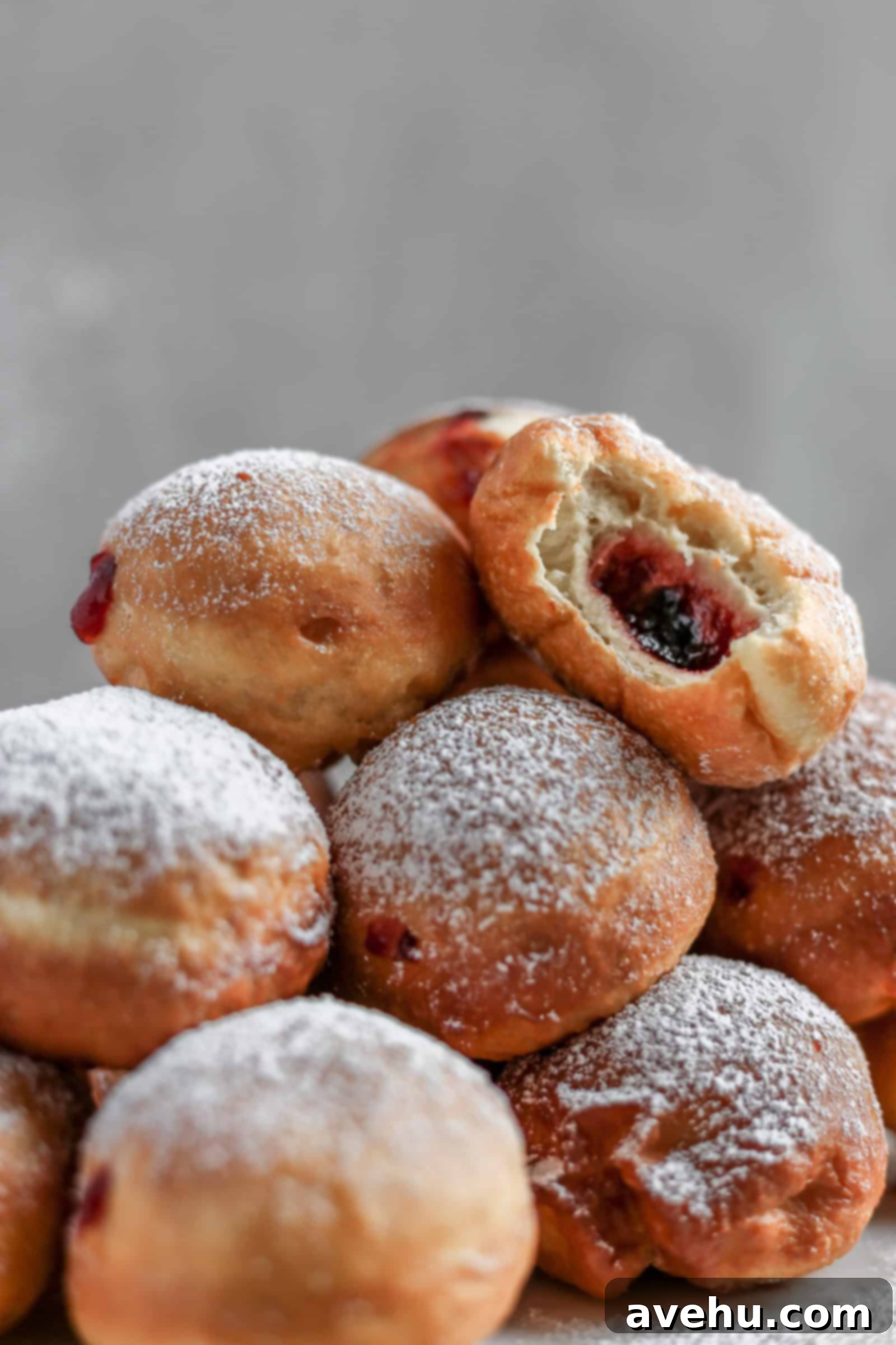 Pillowy Hanukkah Jelly Donuts 3 Fried jelly donuts piled on top of each other with a bite taken out of the top one.