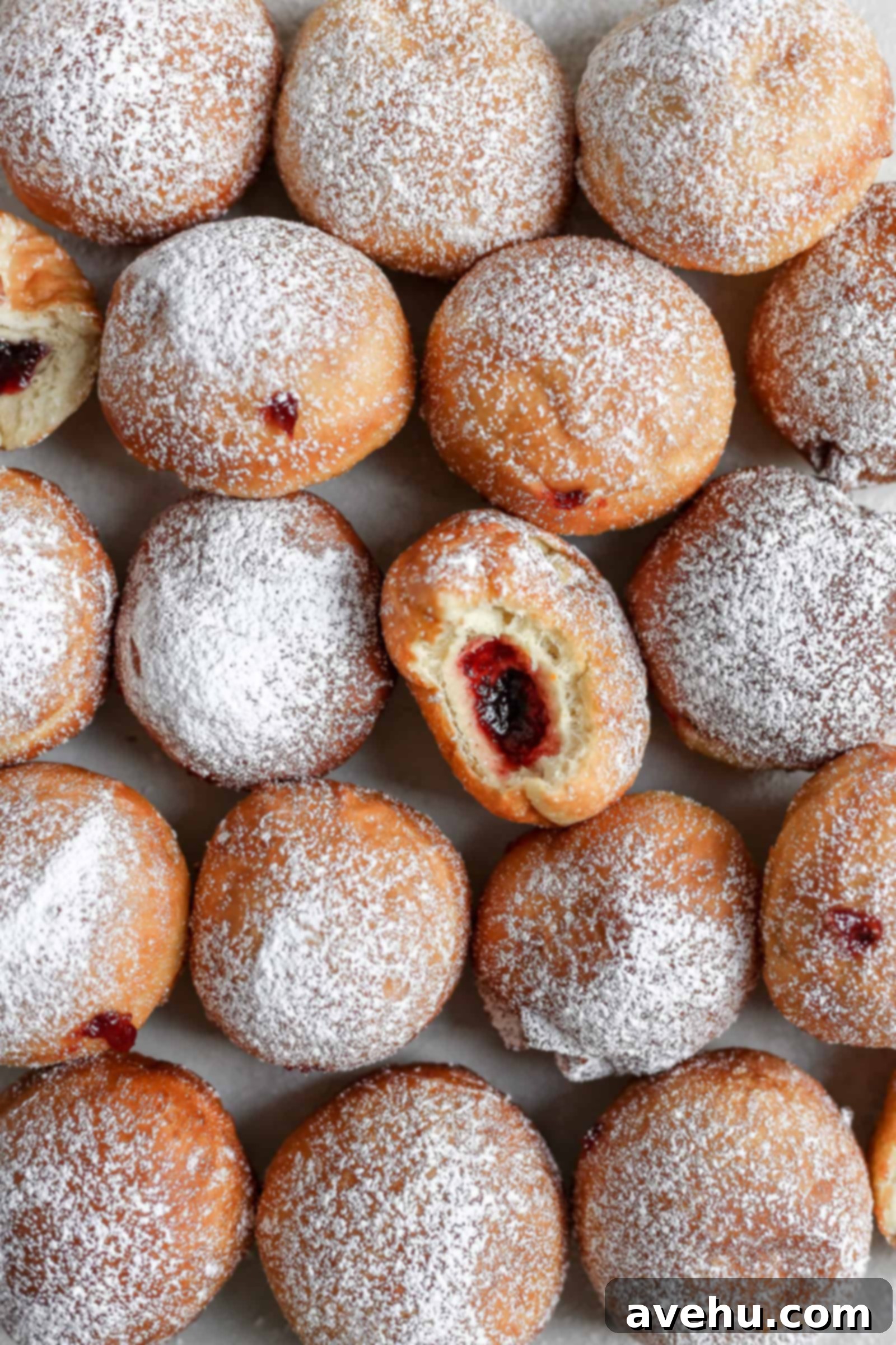 Pillowy Hanukkah Jelly Donuts 4 fried jelly donuts laid out on grey background with a bite taken out of one of them.