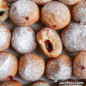 Pillowy Hanukkah Jelly Donuts 5 fried jelly donuts laid out on grey background with a bite taken out of one of them.