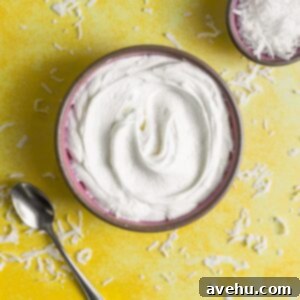 Quick & Creamy Coconut Frosting 2 An overhead view of white frosting in a pink bowl on a yellow surface surrounded by shredded coconut.