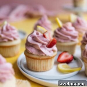 A strawberry lemon cupcake sitting on a white plate on a yellow surface.