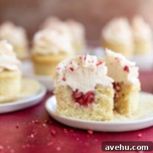 A cupcake sliced in half to reveal the strawberry filling inside on a white plate and red surface.