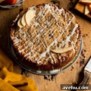 A coffee cake with glaze and sliced apples on a wood surface.