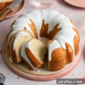 A vanilla bundt cake with slices cut out of it on a pink plate.