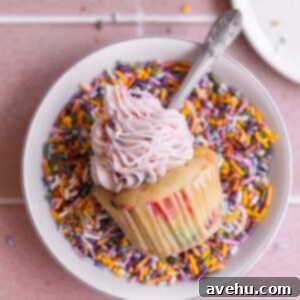 One confetti cupcakes on its side in a bowl of sprinkles.