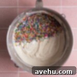 Vanilla cake batter topped with sprinkles in a mixing bowl.