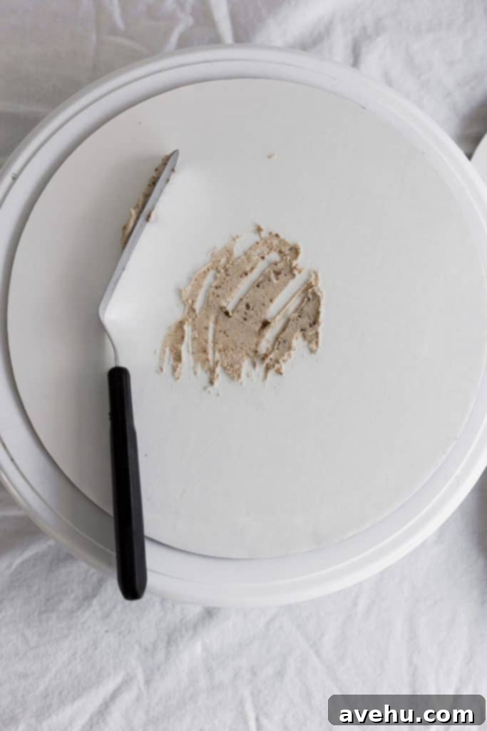 Elevate Your Cakes To Pro Level: 10 Essential Techniques 5 A cake board with frosting dabbed on to the middle and an offset spatula set to the side